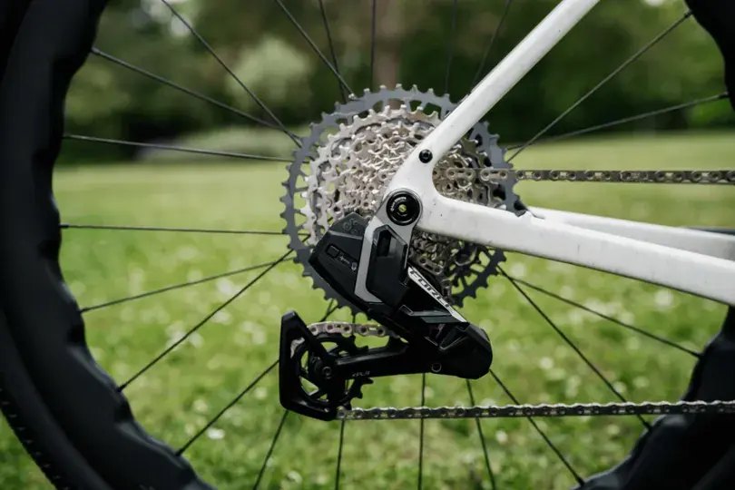 Nahaufnahme der Hinterachse eines weißen Gravelbikes mit schwarzen Zinken, Zahnrad und Kettenschaltung auf grünem Rasen im Hintergrund.