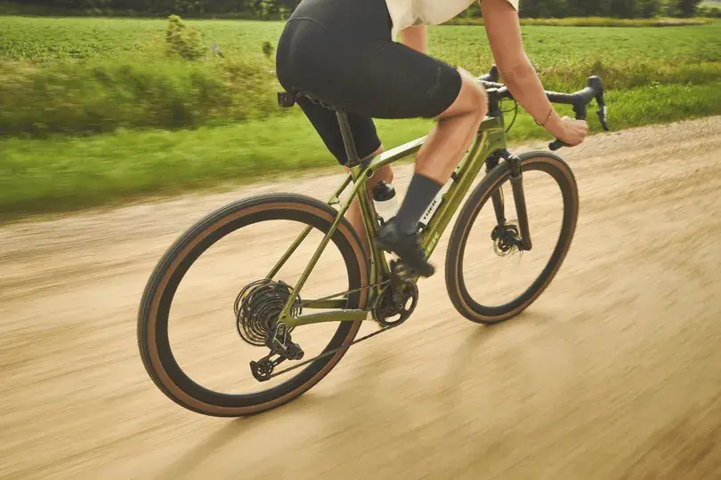Gravelbike fährt über Schotter in einer grünen Landschaft.