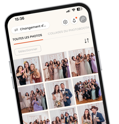 Vue rapprochée et inclinée d'un smartphone affichant l'interface de l'application mobile KRUU. L'écran affiche une galerie de photos numériques intitulée "Alle Bilder" (Toutes les images) remplie de diverses photos de groupe prises lors d'un mariage. Les photos montrent des invités en tenue de soirée qui posent avec des accessoires amusants tels que des verres en forme de cœur et des panneaux "Just Married". Le design de l'application est propre et moderne, avec des icônes de navigation pour les paramètres, les notifications et le partage en haut de l'application.