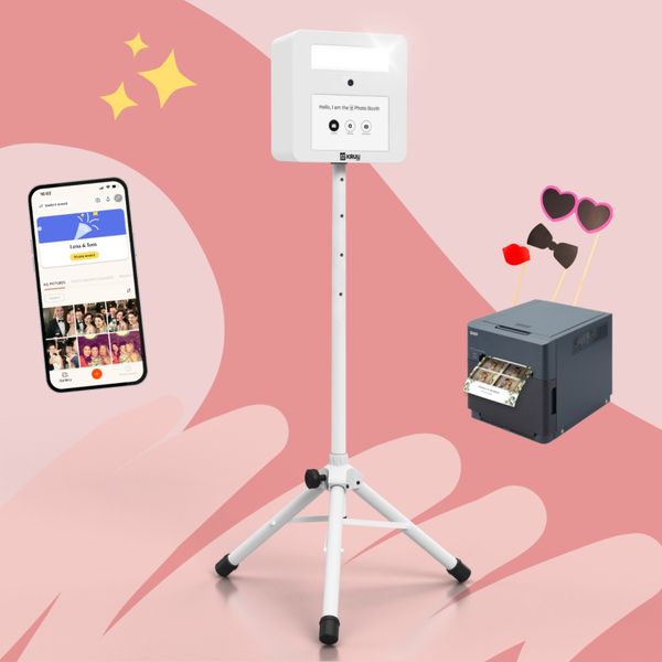 KRUU Photo Booth on a stand, alongside a mobile phone showing the KRUU App and a highspeed printer with photo props, against a pink background.