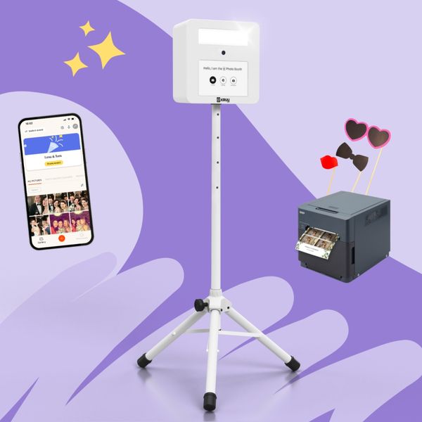 KRUU Photo Booth setup on a stand, with a mobile phone displaying the KRUU App and a highspeed printer with photo props, all on a purple background.