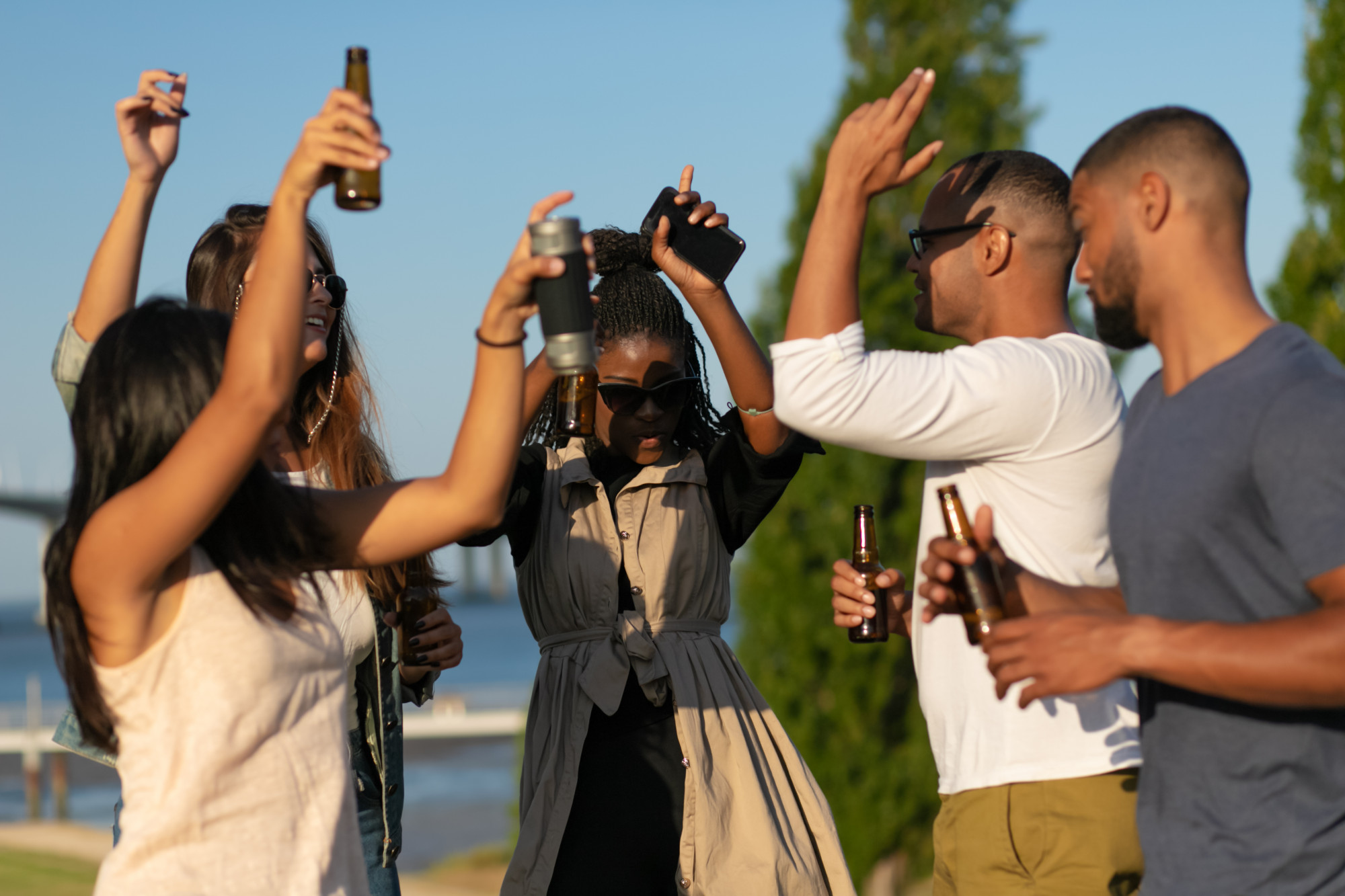Group of friends dancing and enjoying drinks outdoors on a sunny day.
