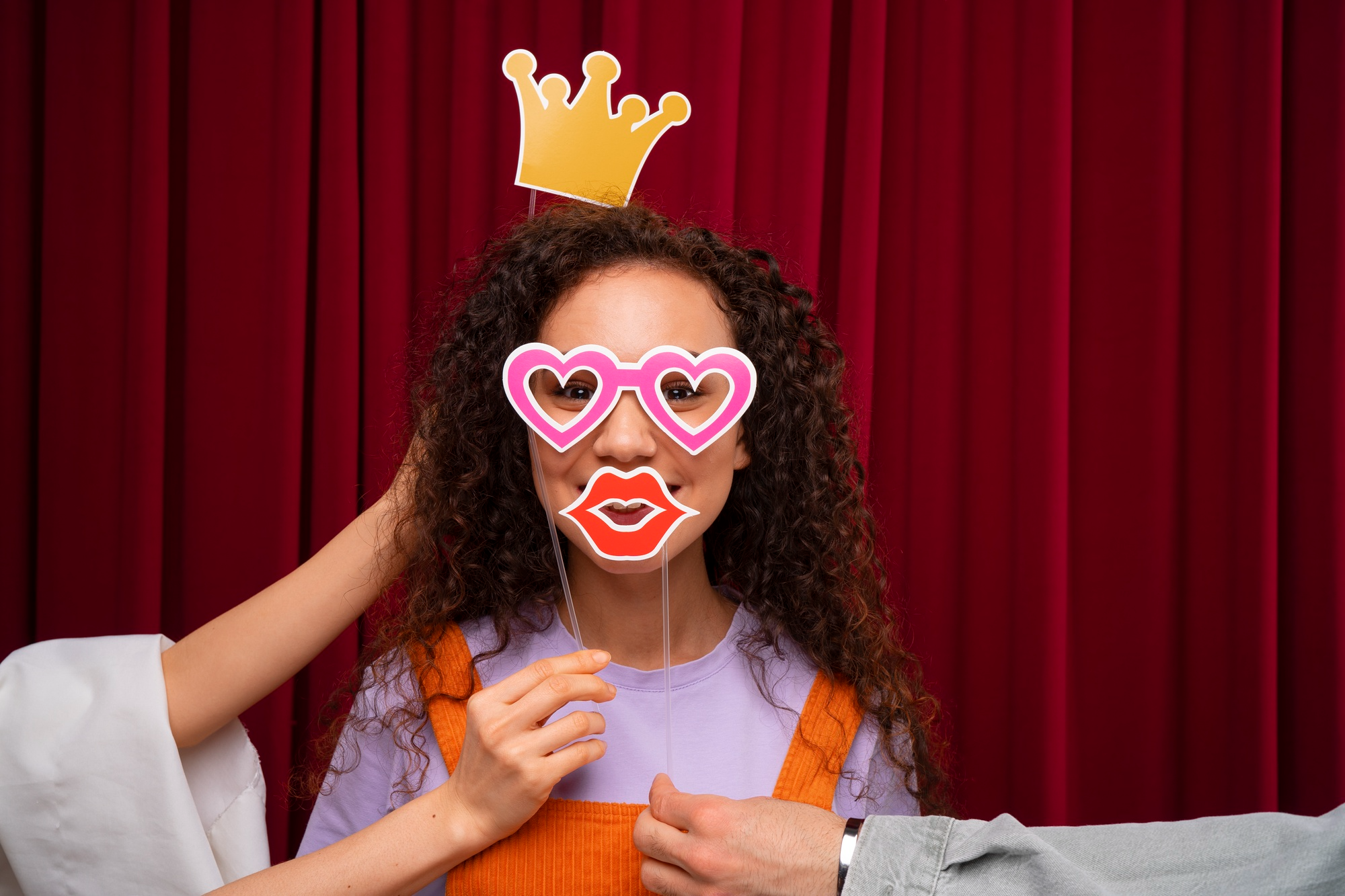 Young woman posing in front of the Photo Booth with props she is holding herself and additional props held by her friends.