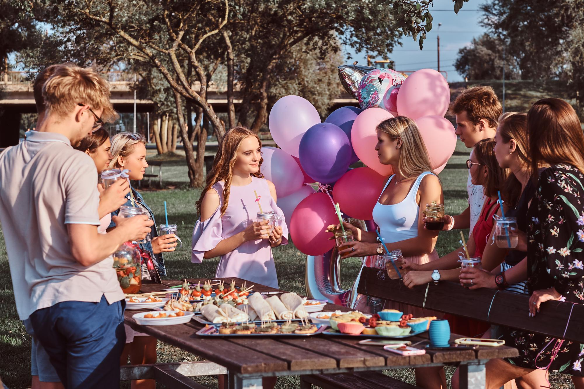 Group of people gathered in a park with colorful balloons in the background, enjoying a cheerful and relaxed atmosphere.