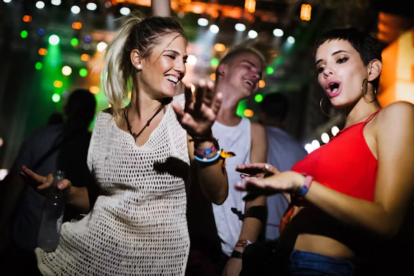 Music festival fun: Happy friends dancing at night concert. Energetic young crowd enjoying live music & party lights.