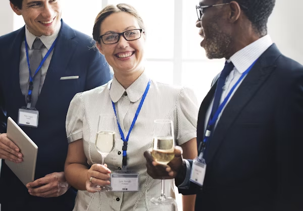 Corporate Event: 3 happy people networking. Smiling professionals with wine & tablet at business gathering.