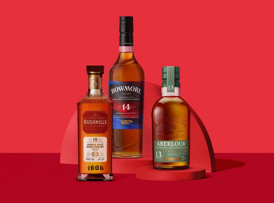 Three whiskey bottles displayed against a red backdrop: Bushmills 10, Bowmore 14, and Aberlour 13, each on red platforms.