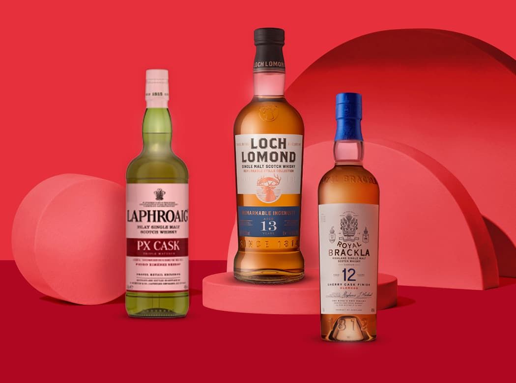 Three bottles of whiskey, including Laphroaig, Loch Lomond, and Royal Brackla, on a red background with circular podiums.