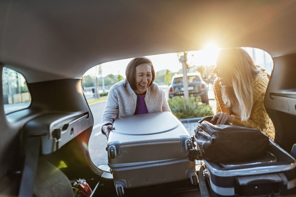 Two women laughing taking suitcases out of boot