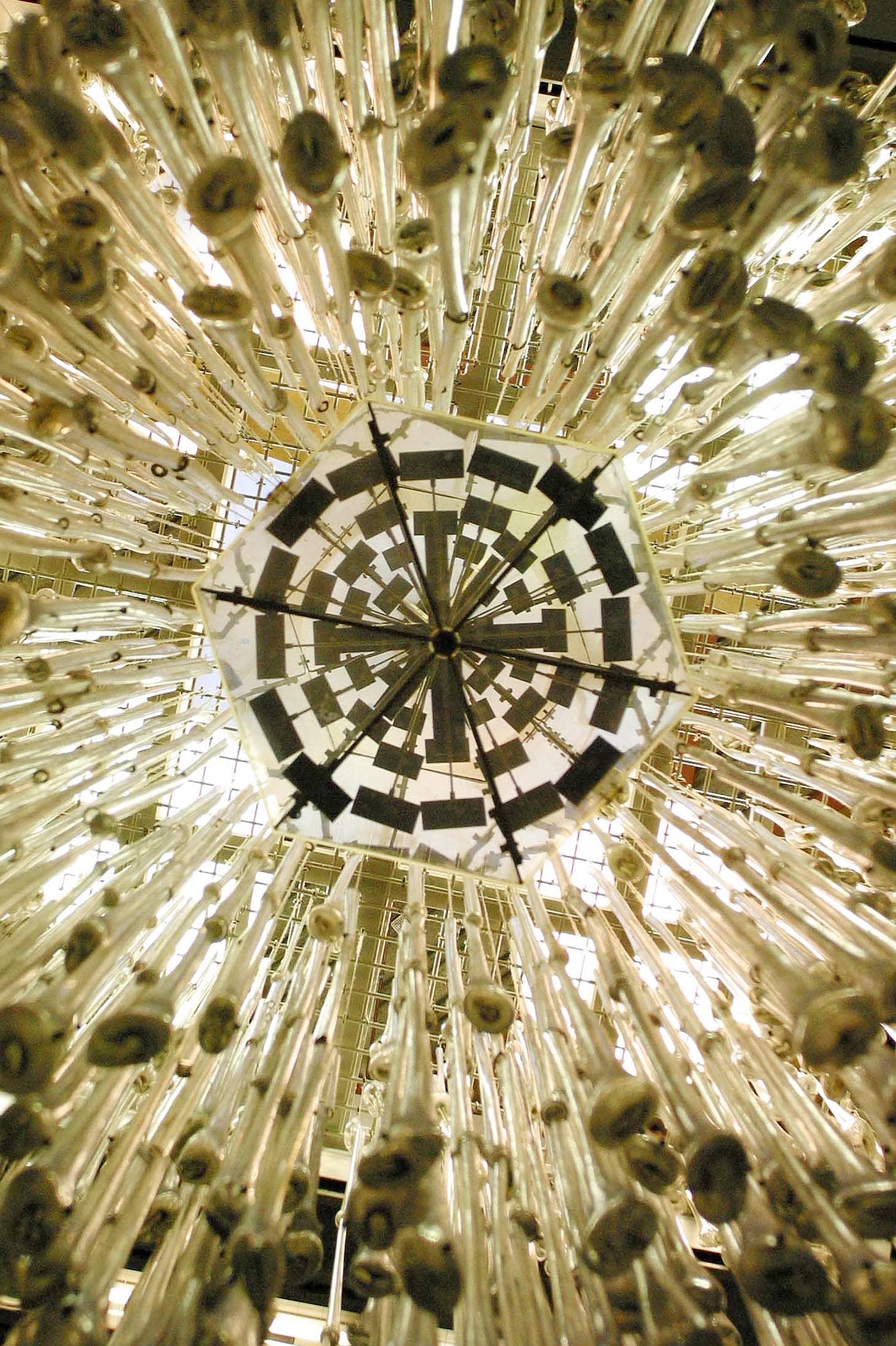 Looking up at a chandelier with numerous hanging glass tubes and a geometric, mirrored centrepiece.