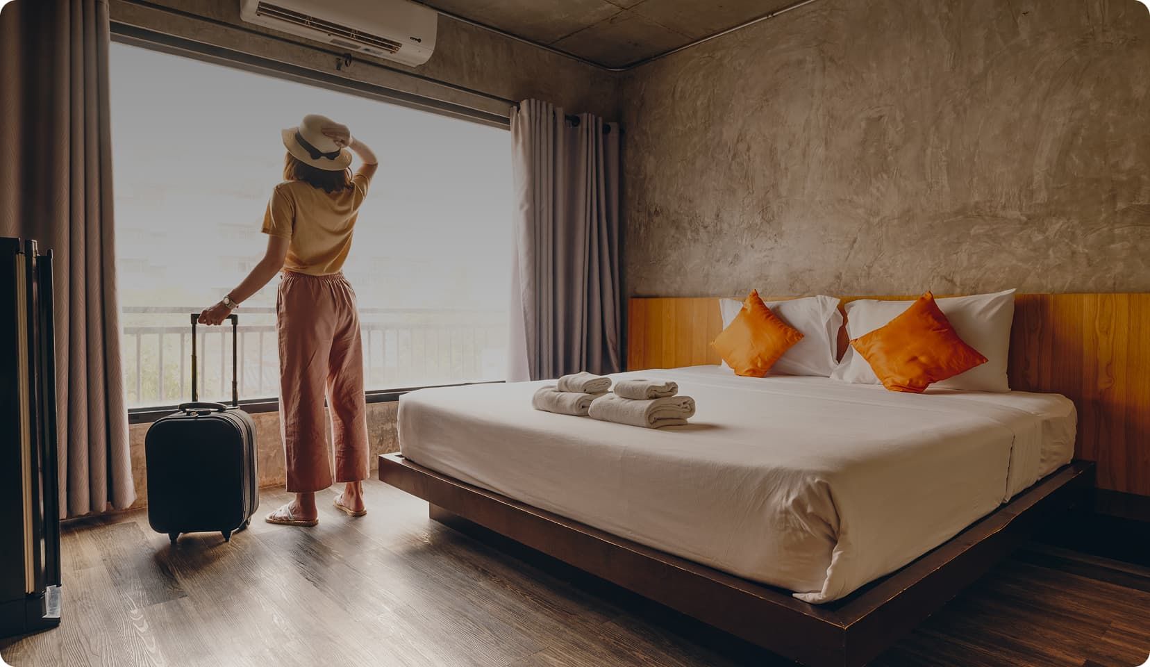 Woman looking outside of hotel room with suitcase