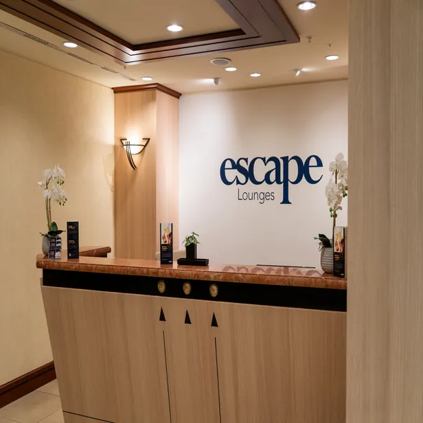 Reception desk of Escape Lounges with promotional brochures and orchids, under warm lighting.