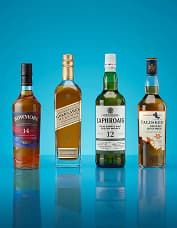 Four whisky bottles on a blue background, featuring different label designs and colors, displayed in a row.