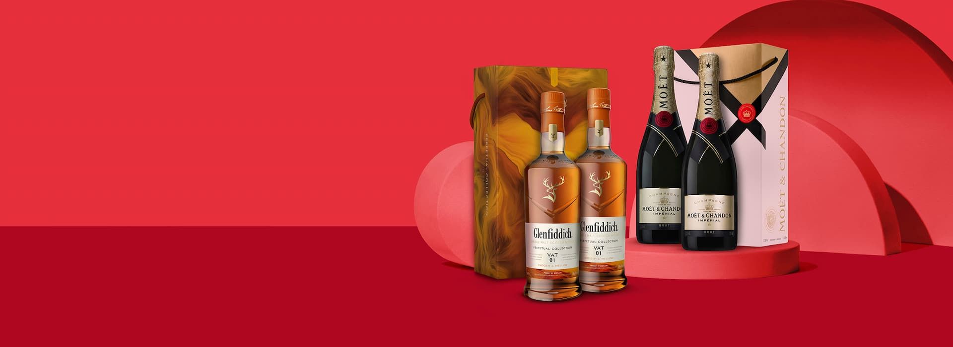 Assorted whisky and champagne bottles with decorative boxes against a red backdrop.