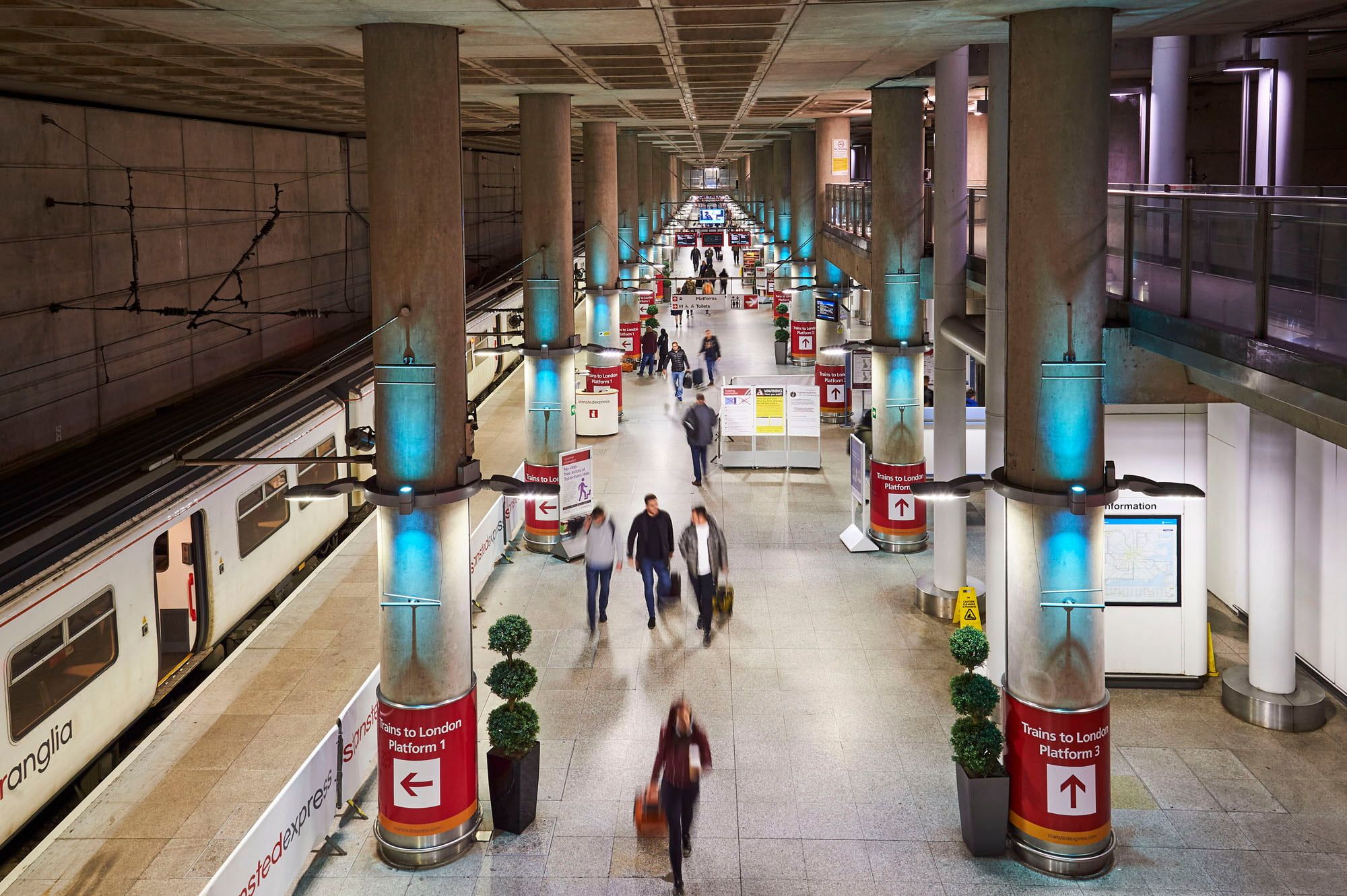 Busy underground train station platform with passengers walking, signs directing to London, and a train on the left.