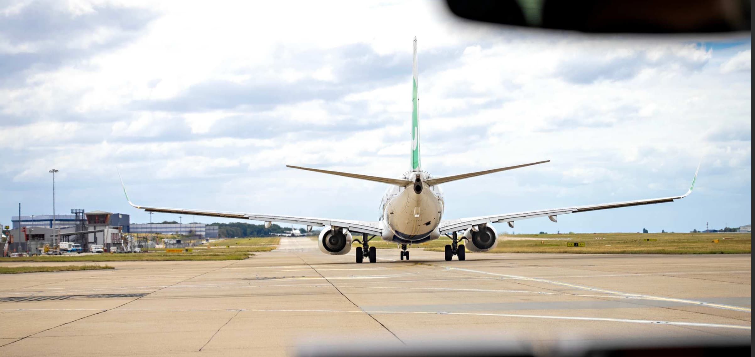 Airplane taxiing on runway under cloudy sky, with airport buildings visible in the background.