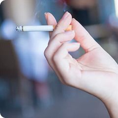 Hand holding a lit cigarette with a blurred background.