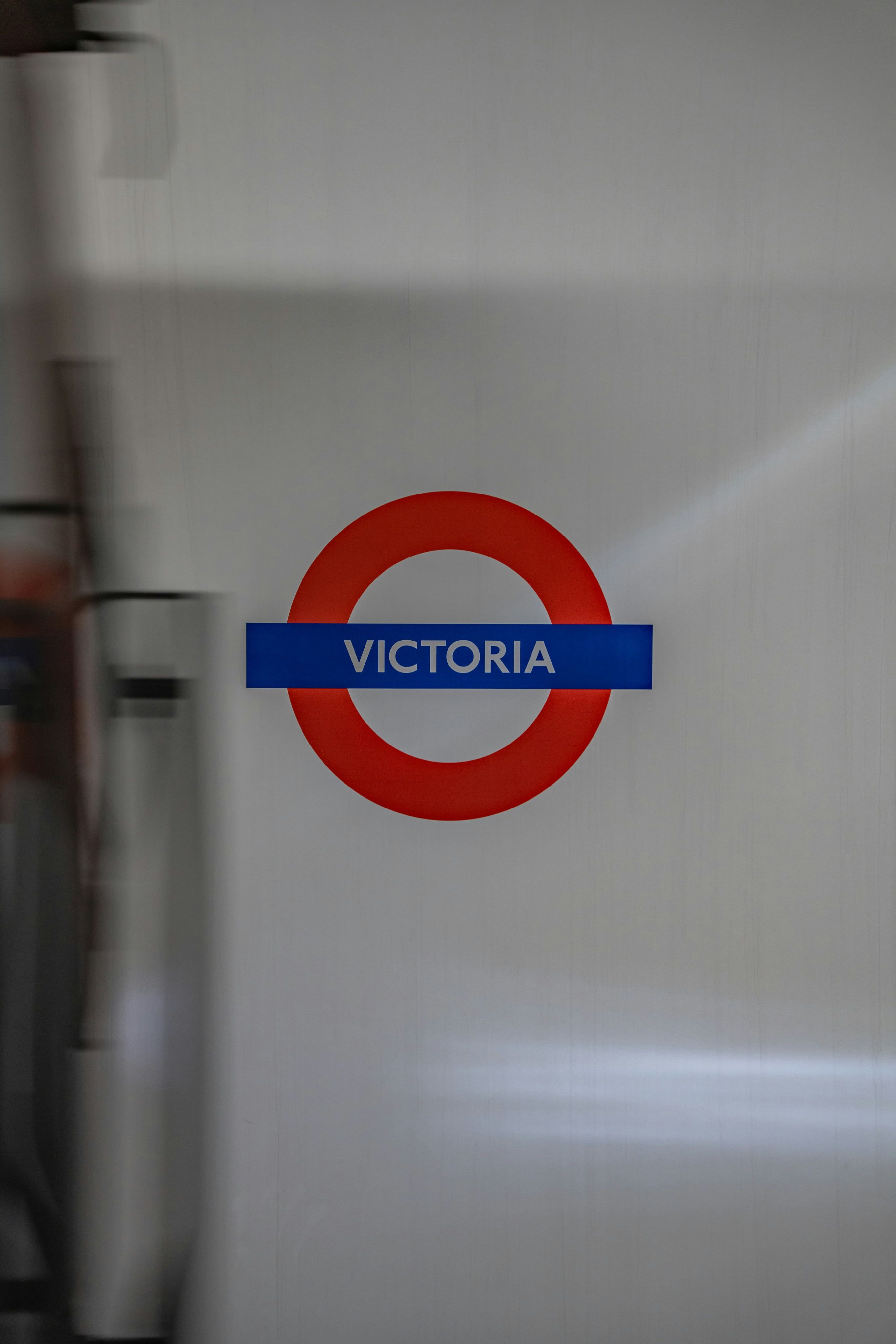 Red and blue Victoria Underground station sign on a white wall, with a blurred motion effect on the left side.