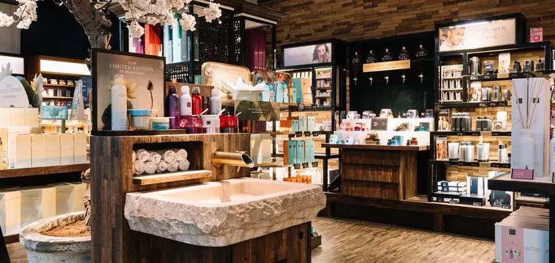 Luxurious skincare store with wooden décor, a stone sink, flower arrangements, and well-organised shelves of products and towels.