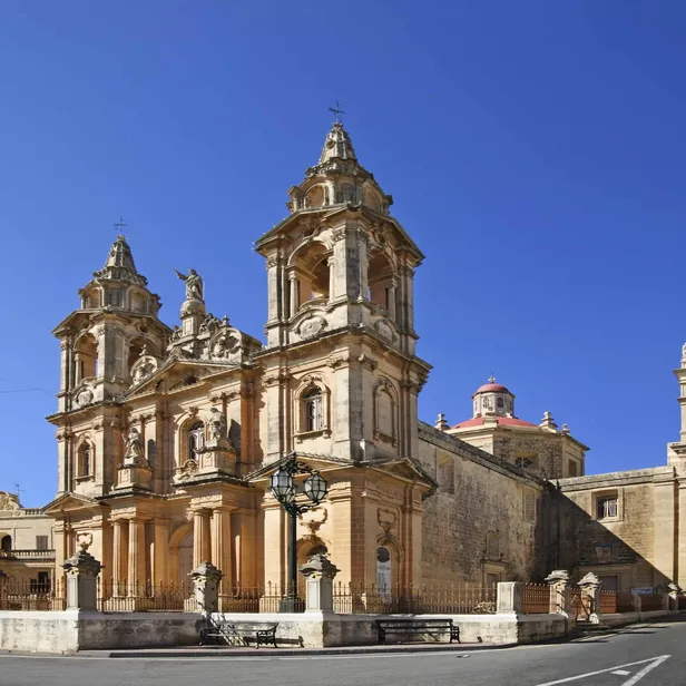 Historic church with ornate architecture, twin bell towers, and a central dome, set against a clear blue sky.