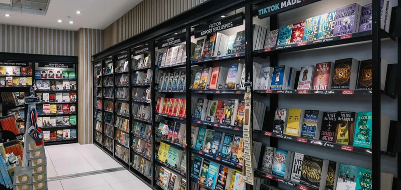 Bookshelves in a store display various books under sections like "Non-Fiction," "Fiction Airport Exclusives," and "TikTok Made Me Buy It."