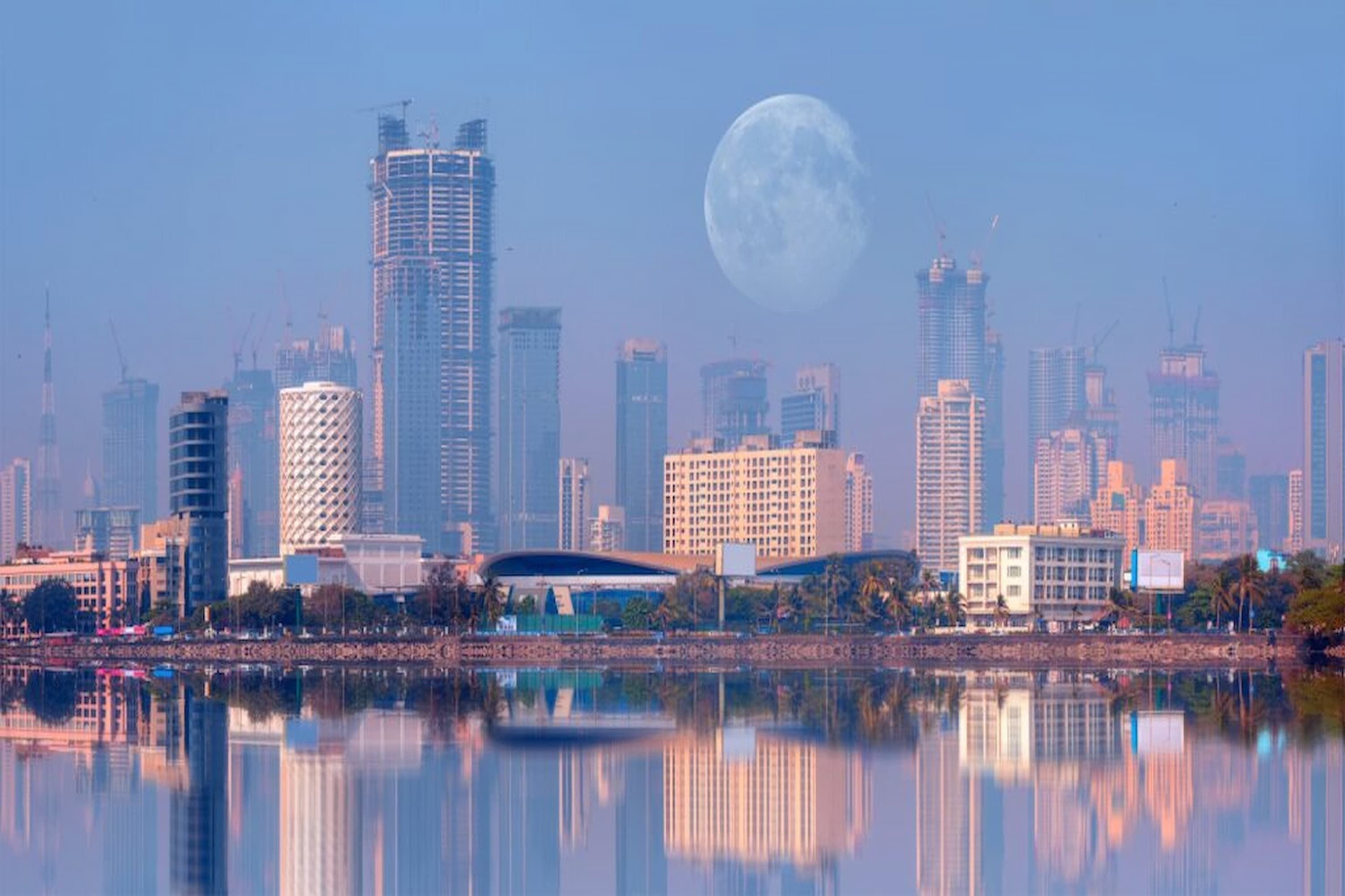 City skyline with modern skyscrapers at dawn, a large moon visible in the sky, and serene water reflections in the foreground.