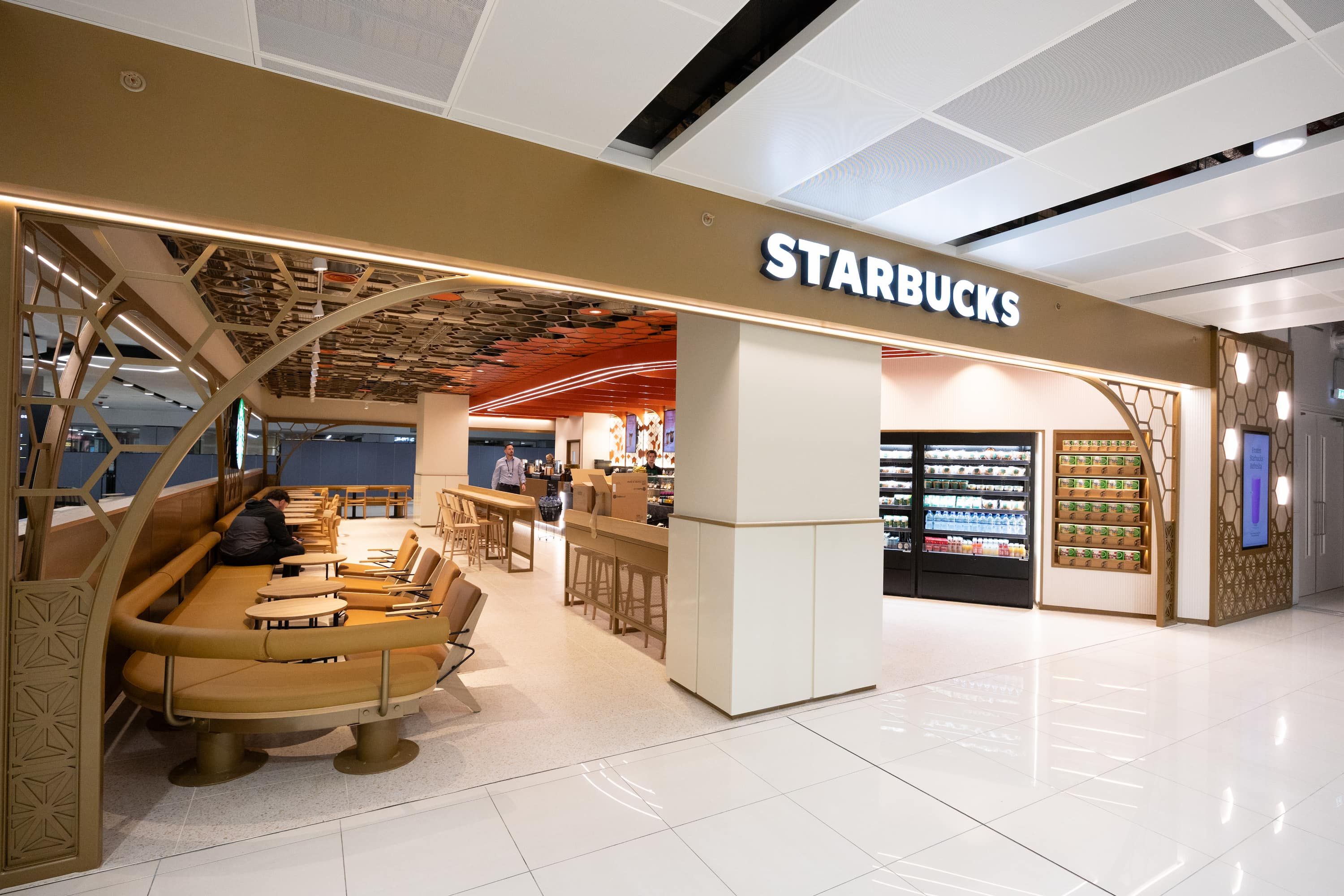 A modern Starbucks with seating area, counter, and beverage displays, featuring stylish lighting and decor in a bright, open space.