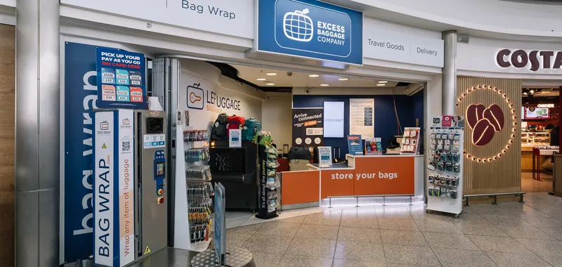 Excess Baggage Company store in an airport offers bag storage, wrapping services, and travel goods. Nearby is a coffee shop with a bright logo.