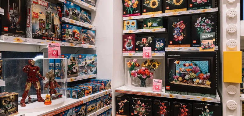 A store shelf filled with various LEGO sets, including Marvel figures and botanical designs, with colourful displays of LEGO flowers.