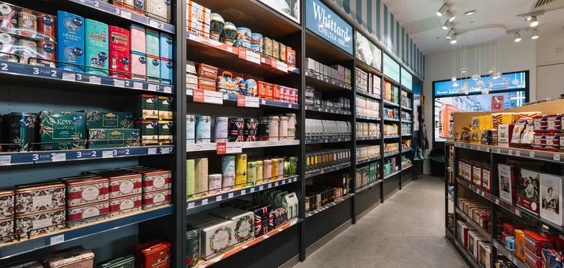 A store aisle filled with assorted tea tins and boxes on shelves. Signs display offers like "3 for 2" and "Low Price" under bright lighting.