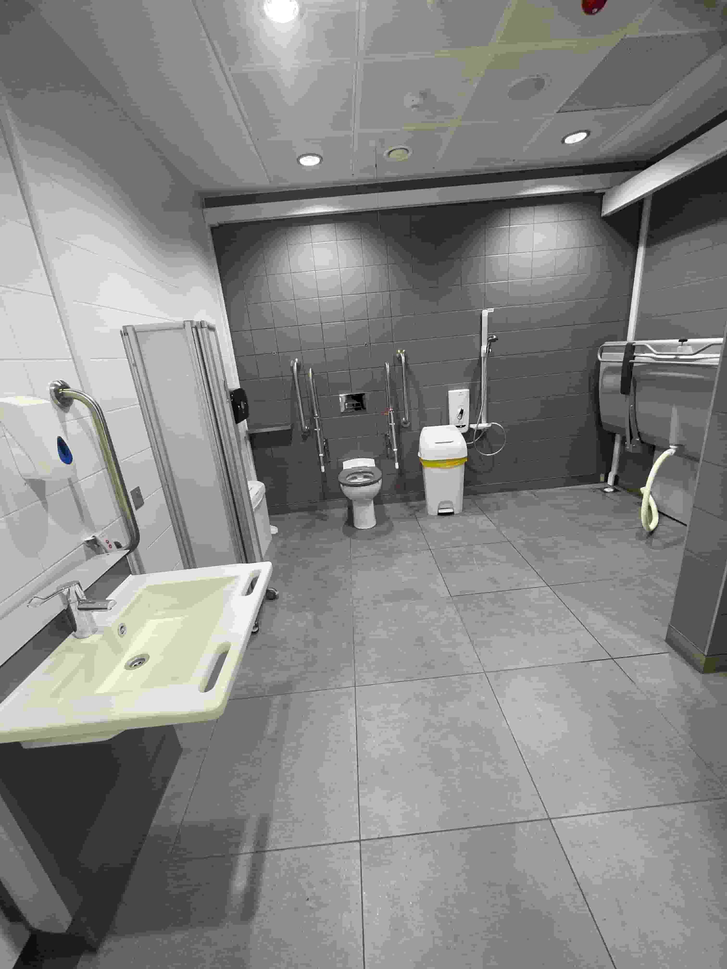 Accessible restroom with a wall-mounted sink, grab rails around a toilet, a hand dryer, and cleaning equipment.
