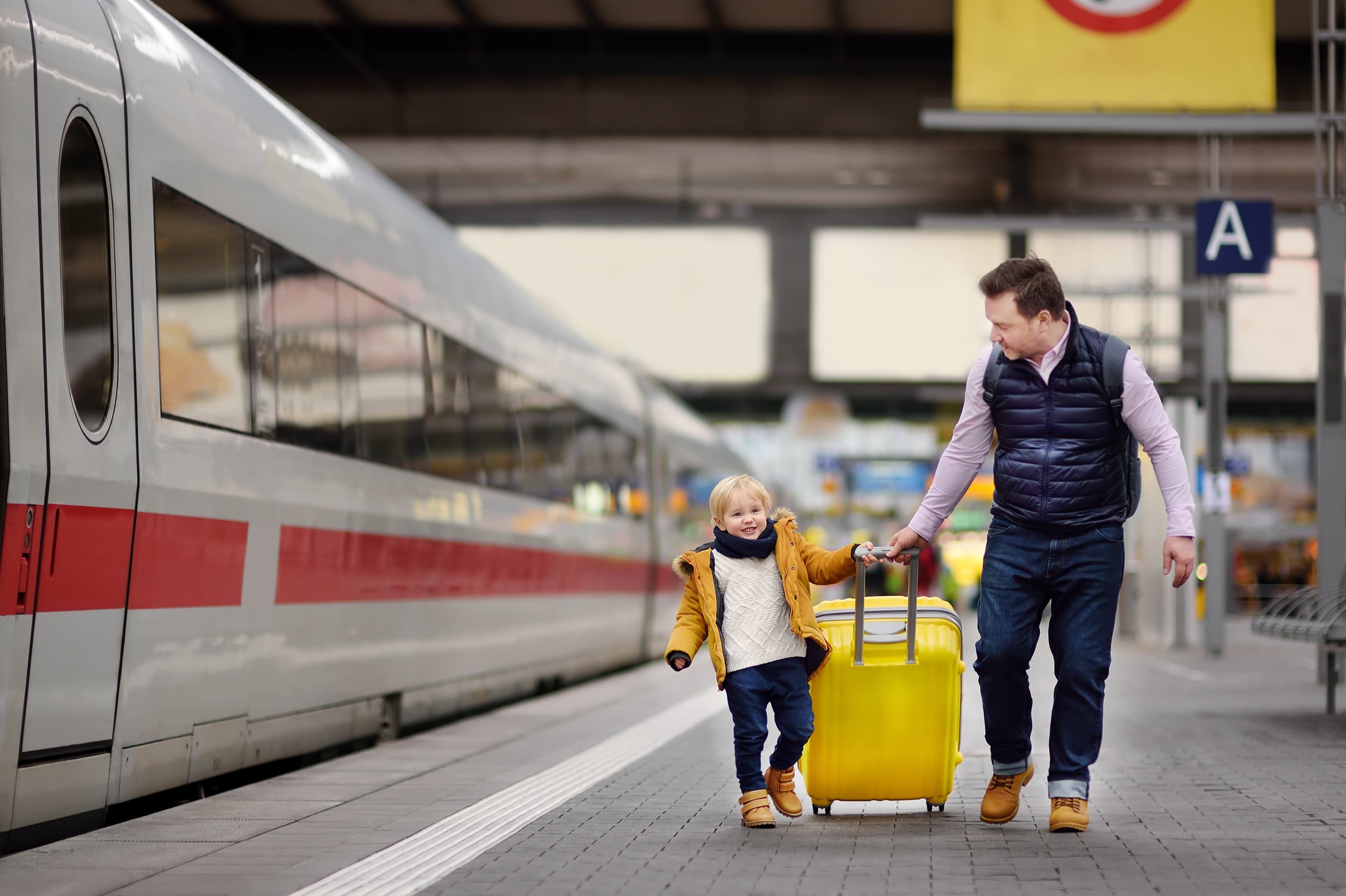 Man and little boy walking alongside train pulling suitcase