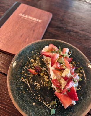Colourful food on plate next to menu that says Alembic