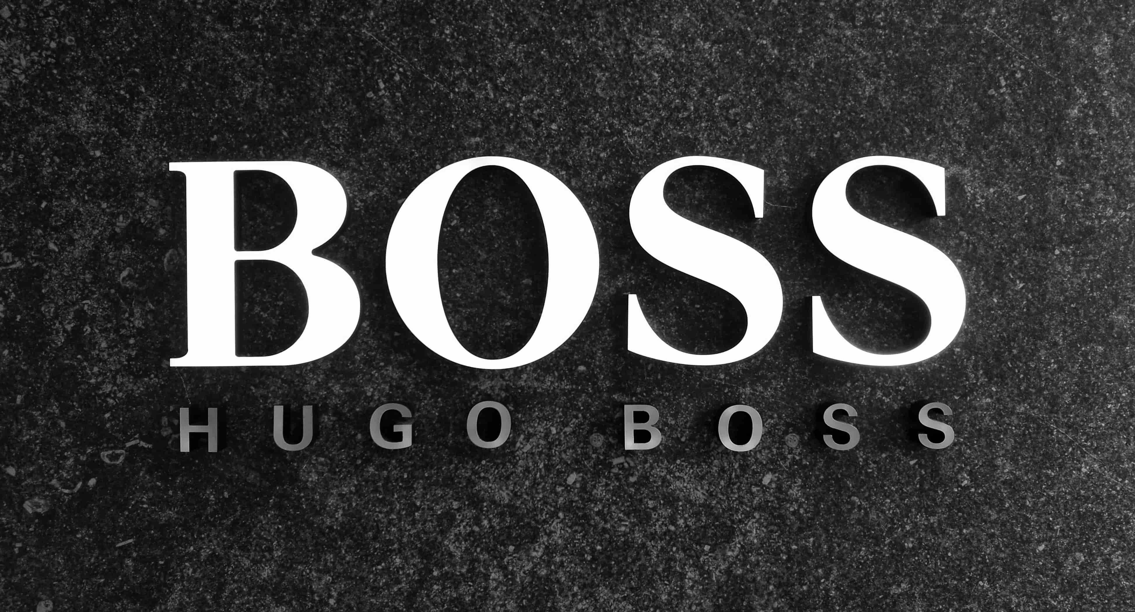 Hugo Boss logo: large white "BOSS" text with smaller "HUGO BOSS" beneath on a dark, textured stone background.