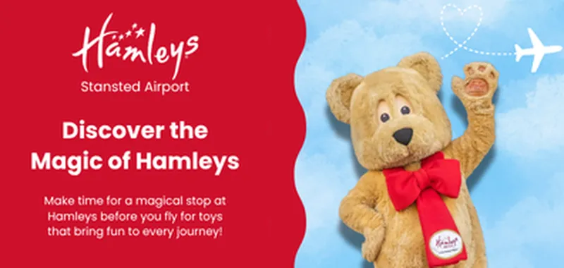 A smiling teddy bear with a red bow and Hamleys badge waves beside text about visiting Hamleys at Stansted Airport, with a plane flying in the sky.