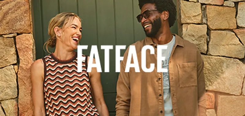 A woman and a man are smiling and laughing together in front of a stone wall, with the word "FATFACE" overlaid on the image.