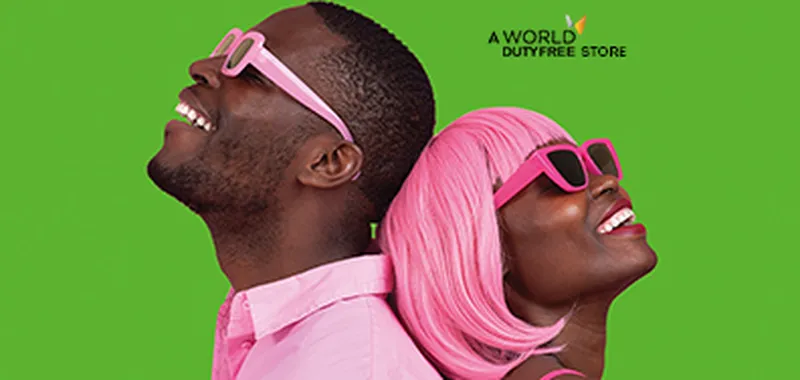 A man and woman, both wearing pink sunglasses, lean back-to-back against a green background, smiling joyfully.