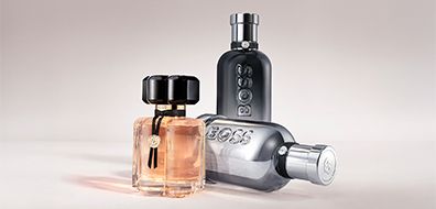 Three Boss perfume bottles showcase on a light background: a pale pink, black, and metallic design, each with distinct shapes and elegant branding.