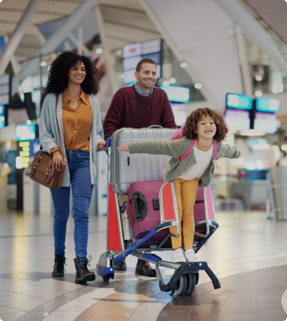 Family walking through airport with suitcase and child on trolley