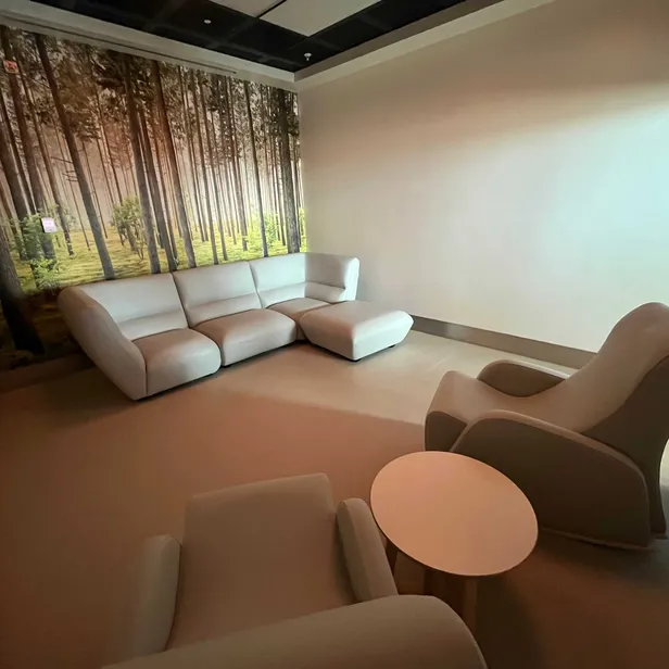 Modern room with white sofas and chairs, a small round table, and a wall mural of a serene forest scene.