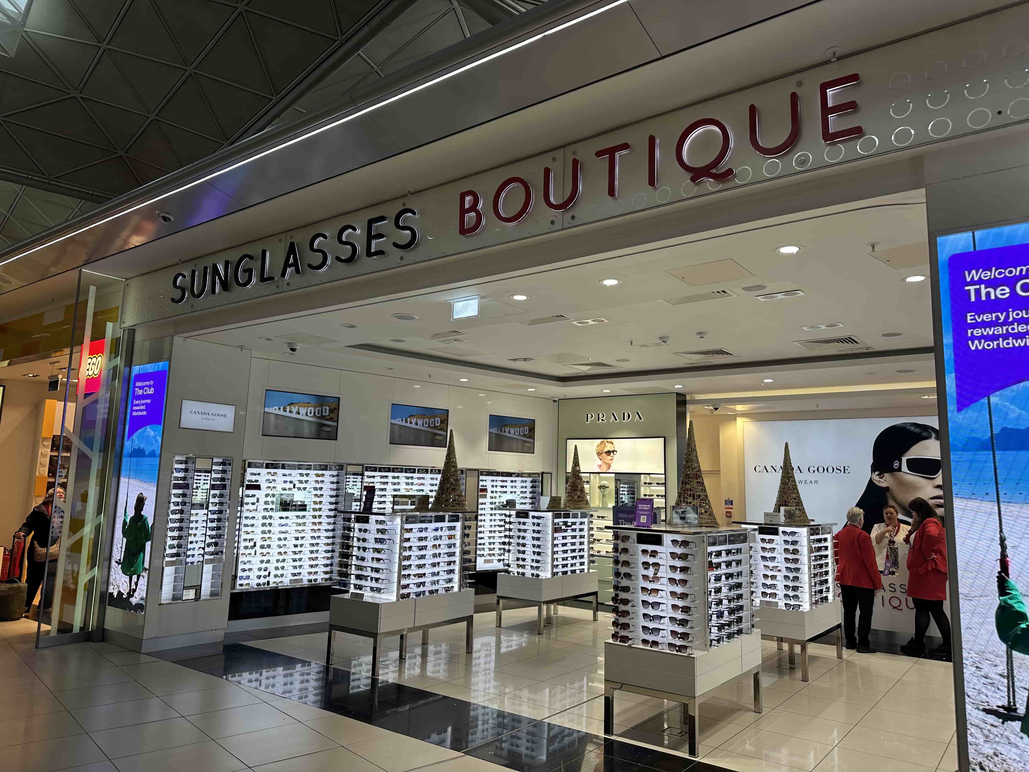 Airport Sunglasses Boutique interior with illuminated display towers of sunglasses, Prada signage and staff near the back.
