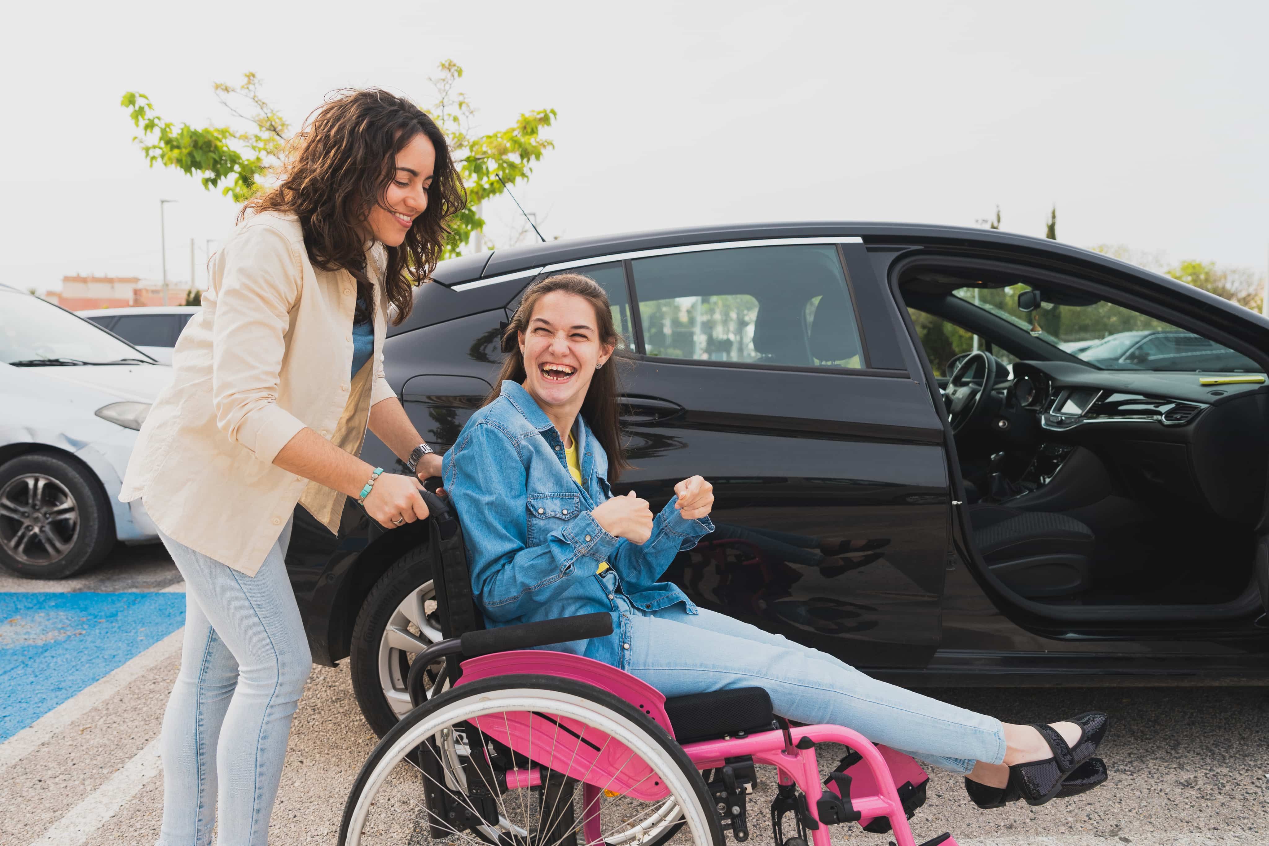 Woman pushing girl in wheelchair next to car