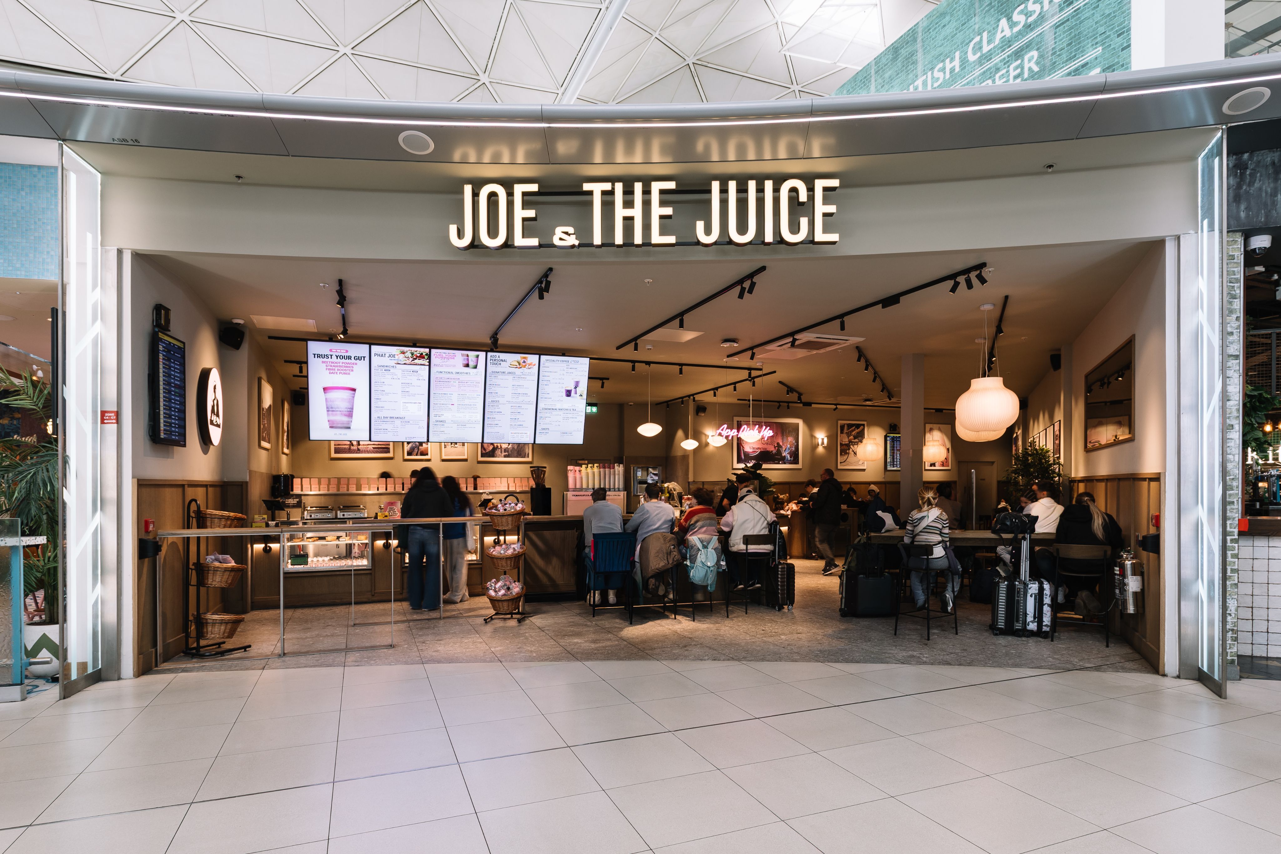 People sitting inside a Joe & The Juice café with a large menu display and soft lighting, creating a cosy atmosphere.