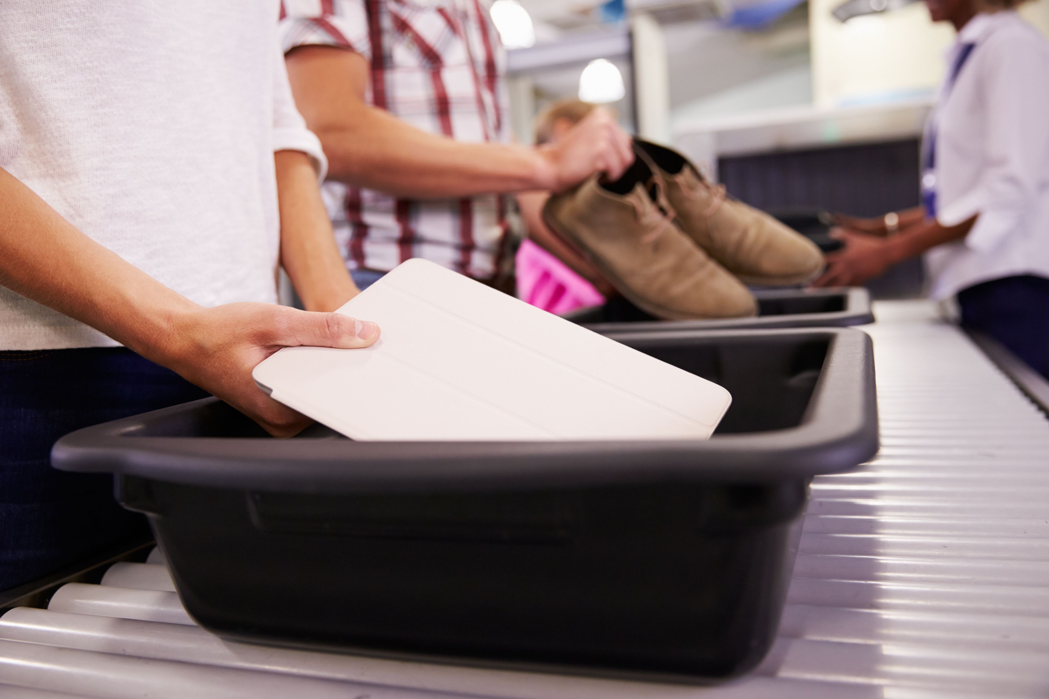 person placing a tablet inside a tray at airport security