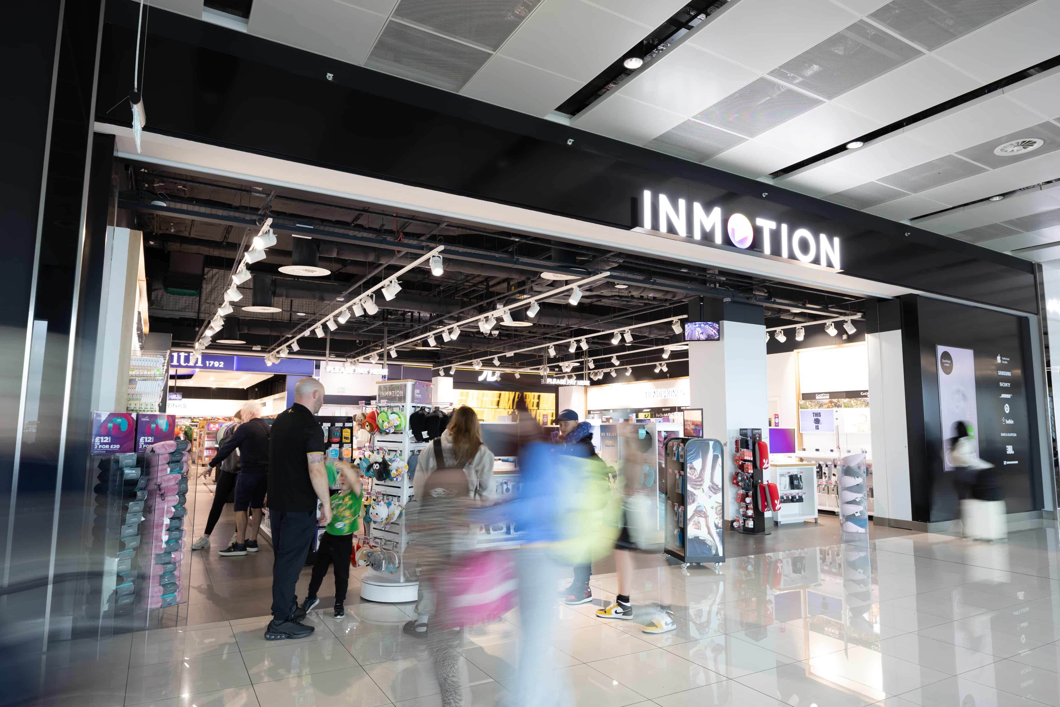 People shopping at an InMotion store in an airport, showcasing electronics and travel accessories under bright lighting with a sleek design.