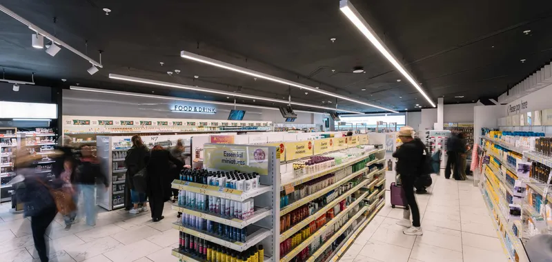 People browse aisles in a brightly lit shop with shelves stocked with health and beauty products.