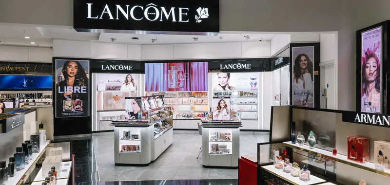 Lancome store interior featuring cosmetics and perfumes, with illuminated displays and promotional posters on white and black fixtures.
