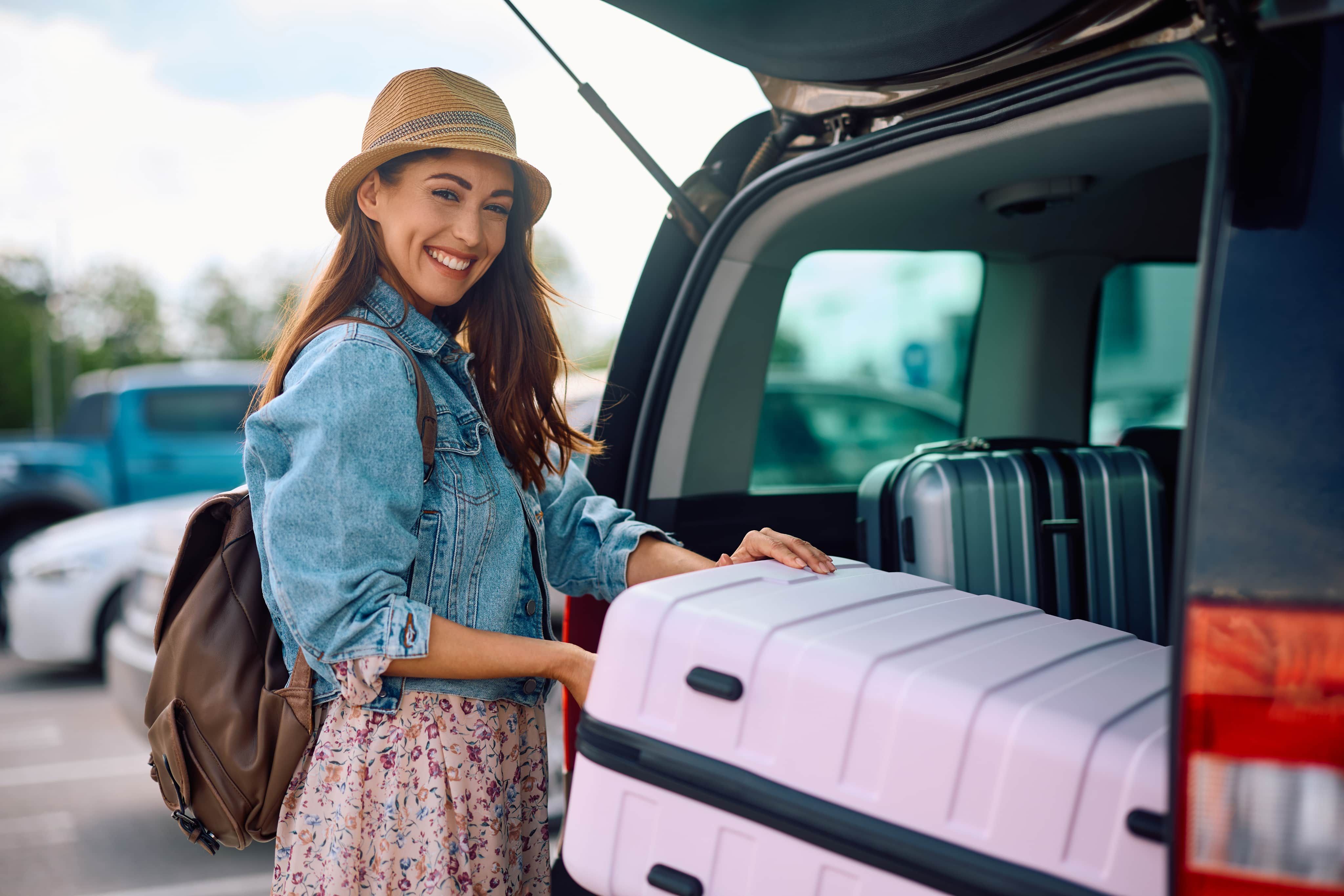 Woman getting pink suitcase out of car boot