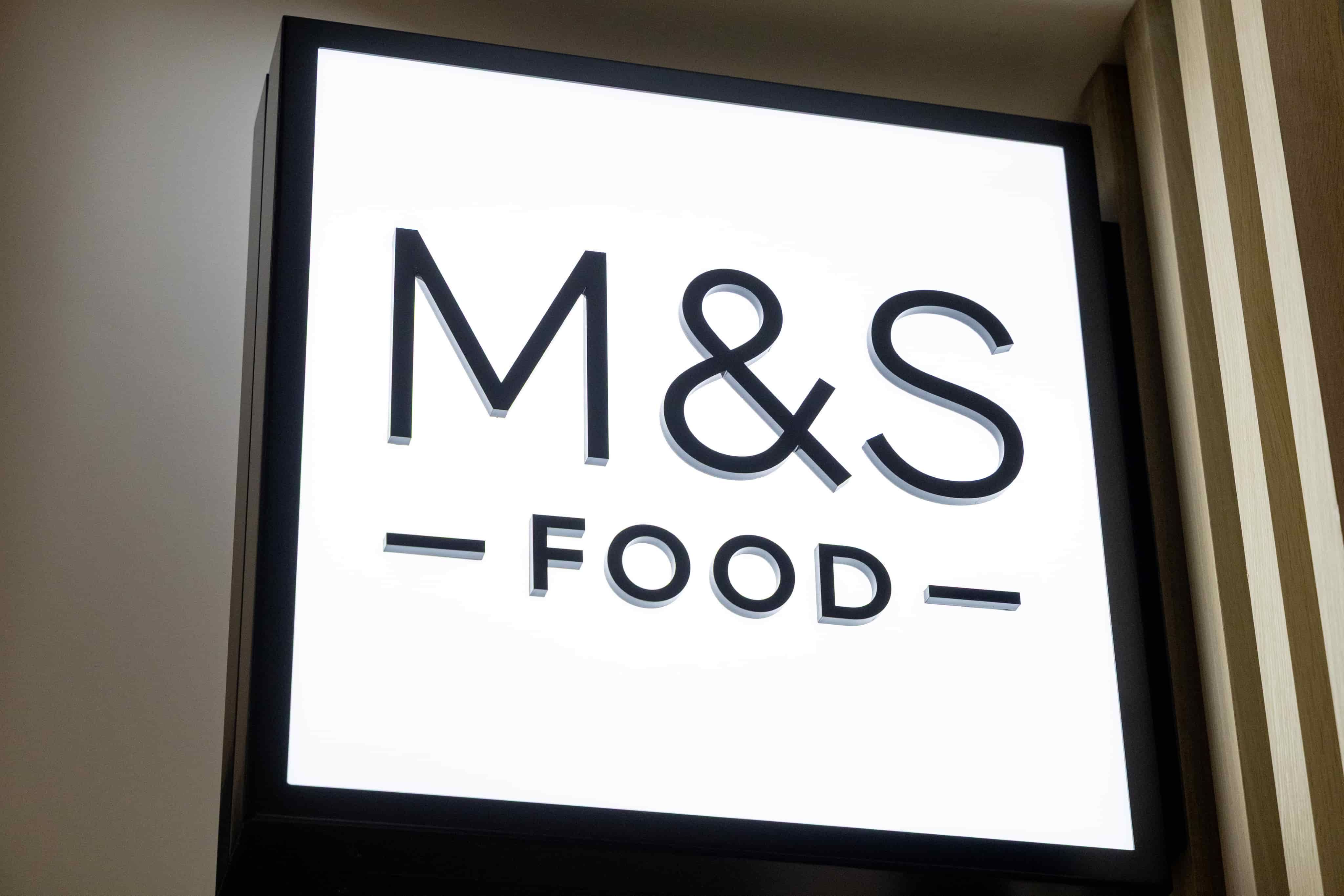 Illuminated "M&S Food" sign with bold black lettering on a white background, mounted on a wall.