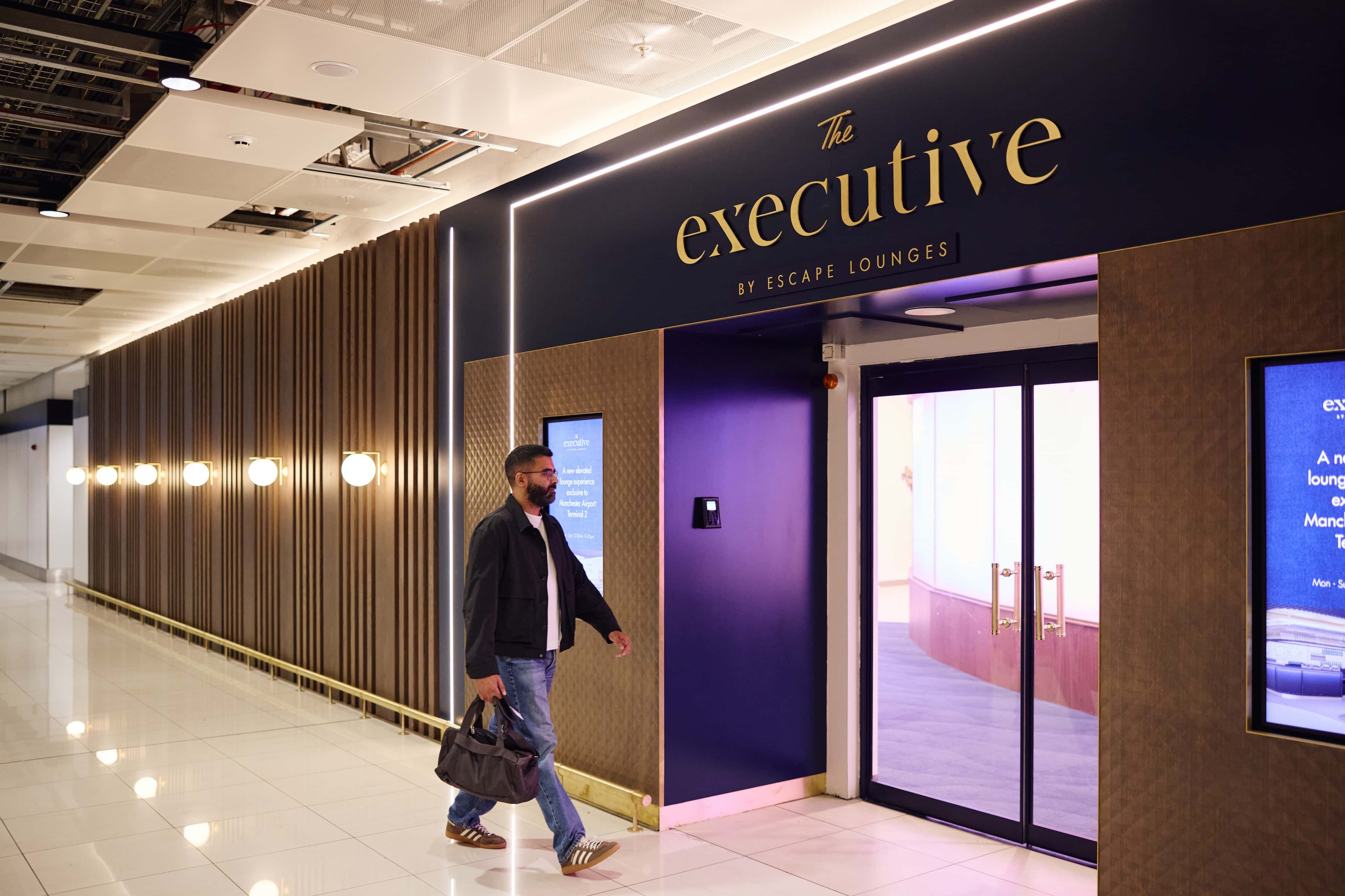 A person with a bag walking towards the entrance of "The Executive" by Escape Lounges, featuring modern lighting and a sleek design.